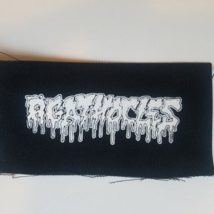 May include: Black rectangular patch featuring the white text "REGURGITATION" in a dripping font. The patch is made of woven fabric and has a raw edge.