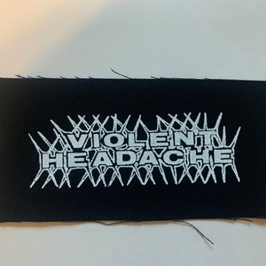 May include: Black fabric patch with white text that reads "VIOLENT HEADACHE" surrounded by a barbed wire design.
