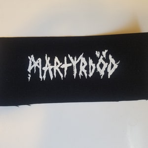Puede incluir: Parche de tela negro con letras blancas que dicen "MARTYRÖD".