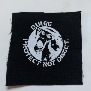 May include: Black square patch with white text and graphic. The text reads "DIRGE" above a white circle with a graphic of a creature. The text "PROTECT NOT DISECT" is below the graphic.