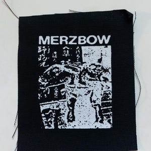 Pode incluir: Etiqueta tecida preta e branca com o texto "MERZBOW" e uma imagem gráfica de uma pessoa em pé em frente a um edifício.