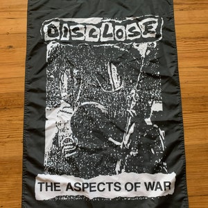 May include: Black and white flag with the band name "DISCLOSE" and the text "THE ASPECTS OF WAR" printed on it.