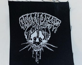 May include: White embroidered patch on black fabric with the text "AGGRESSOR" in a dripping font above a skull with dripping blood.