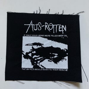 Pode incluir: Patch quadrado preto com texto e gráfico brancos. O texto diz "Aus-Rotten" acima da imagem de um gráfico em preto e branco. Abaixo do gráfico está o texto "If only your veins were filled with oil, the world would rush to your rescue."