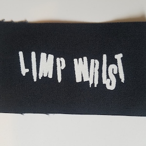 May include: Black fabric patch with the white text "LIMP WRIST" in a stylised font.