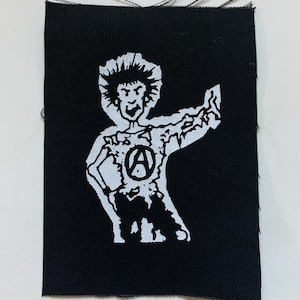 Op de afbeelding: Zwart-witte strijkpatch met een cartoonfiguur met stekelig haar, een grote 'A' in een cirkel op de borst en een opgeheven vuist.