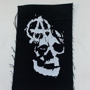 May include: Black and white embroidered patch with a skull and an anarchy symbol.