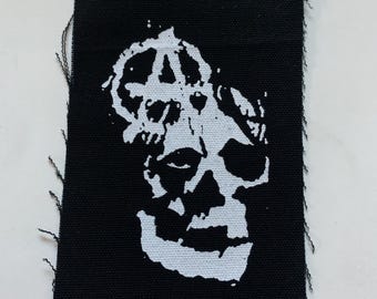 May include: Black and white embroidered patch with a skull and an anarchy symbol.