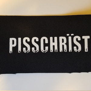 May include: Black fabric patch with white text that reads "PISSSCHRIST".