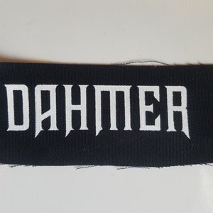Könnte beinhalten: Schwarzer Stoff-Patch mit dem Wort "DAHMER" in weiß gedruckt.