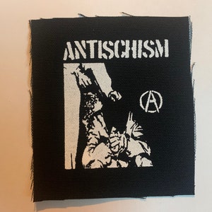 May include: Black and white embroidered patch with the text "ANTISCHISM" and an anarchy symbol. The patch features a stylized image of a person being held down.