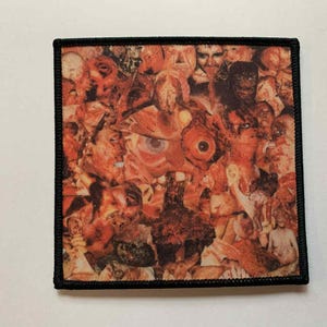 Puede incluir: Parche cuadrado con un collage de rostros y partes del cuerpo en tonos naranja, rojo y marrón. El parche tiene un borde negro. La obra de arte parece ser una composición surrealista o abstracta.