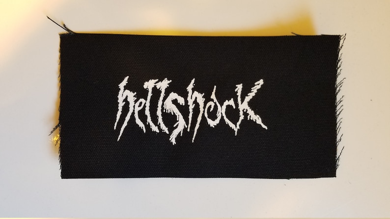 May include: Black fabric patch with white embroidered text that reads "hellshock".