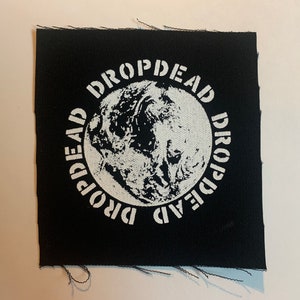 Puede incluir: Parche de tela negro con un círculo blanco que contiene una imagen estilizada de la Tierra y el texto "DROPDEAD" repetido alrededor del círculo.