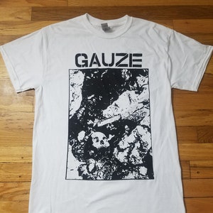 May include: White t-shirt with a black and white graphic print of a skull and bones. The text "GAUZE" is printed in black above the graphic.
