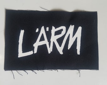 Peut inclure: Un patch en tissu noir avec l'inscription "L'ARM" en blanc dans une police stylisée.