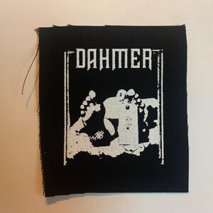 Puede incluir: Parche termoadhesivo blanco y negro con la palabra "Dahmer" y una imagen gráfica de un par de pies.
