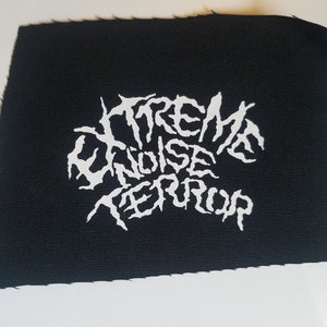 Op de afbeelding: Witte geborduurde patch op zwarte stof met de tekst "EXTREME NOISE TERROR" in een gestileerd lettertype.
