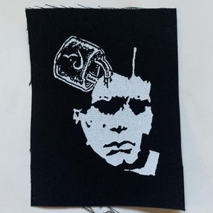 Può includere: Toppa ricamata in bianco e nero di un viso con un lucchetto sulla testa.