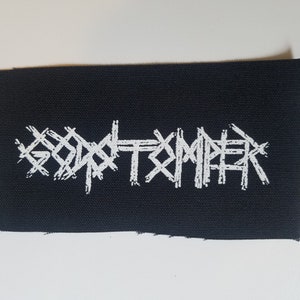 Può includere: Toppa ricamata bianca su tessuto nero con la parola "GODSMACK" in un font stilizzato.