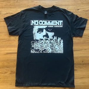May include: Black t-shirt with a white graphic. The graphic includes the words "NO COMMENT" above the words "COMMON SENSELESS". Below the text is a stylized image of a face and figures.