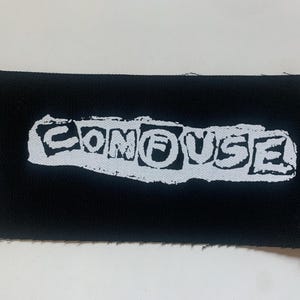 May include: A black rectangular patch with the word "CONFUSE" in distressed white lettering. The text is centered on the patch, which has a raw edge.