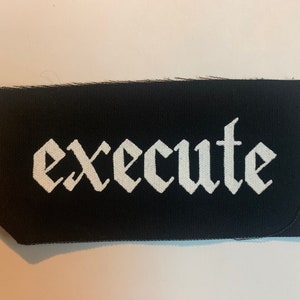 Puede incluir: Parche de tela negro con la palabra "execute" impresa en blanco en una fuente gótica.