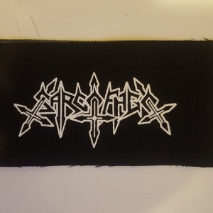 以下が含まれることがあります： 黒い布のパッチに、白い刺繍で「Aether」というロゴがスタイリッシュなフォントで書かれています。