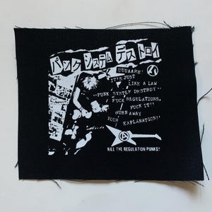 May include: Black square patch with white graphic and text. The design includes Japanese characters, a figure, and phrases like "PUNK SYSTEM DESTROY" and "FUCK REGULATIONS." The patch has frayed edges.