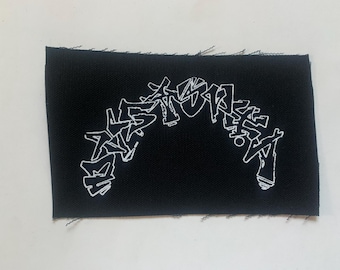 Puede incluir: Parche de tela negro con letras bordadas en blanco que dicen "DESTROY" en estilo graffiti.