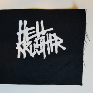 Op de afbeelding: Zwarte stoffen patch met witte tekst "HELL KRUSHER".