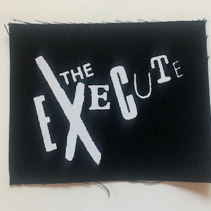 May include: Black fabric patch with white text that reads "THE EXECUTE" with a stylized white X graphic.
