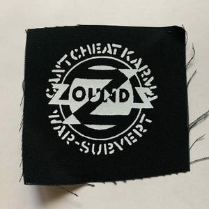 May include: A black square patch with white text and a circular design. The text includes "ZOUND" in a bold font, surrounded by additional text. The patch has frayed edges.