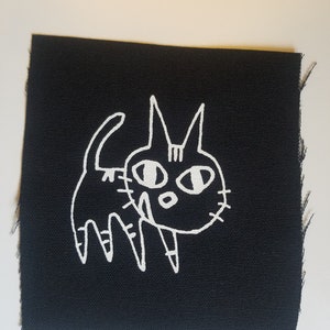 May include: White embroidered cat design on a black fabric patch.