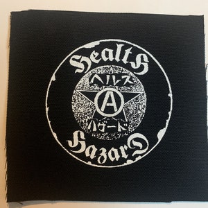 Könnte beinhalten: Ein weißer Patch auf schwarzem Hintergrund mit einem Kreis, der den Text "Sealt's" und "Sazar's" in einer stilisierten Schrift enthält. Im Kreis befindet sich ein Stern mit dem Buchstaben "A" darin und dem Text "ヘイズ" und "ハード" in Japanisch.