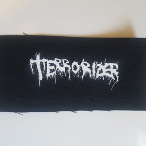 May include: White embroidered patch on black fabric with the word "TERRORIZER" in a stylized font.