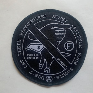 May include: A black and white embroidered patch with the text "DON'T LET THEIR BLOODSOAKED MONEY SILENCE YOUR SHOUTS." The patch features a hand, a dollar sign, and the words "FUCK BIG BUSINESS" and "BOYCOTT."