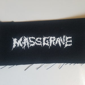 May include: White embroidered patch on black fabric with the text "MASS GRAVE" in a stylized font.