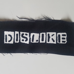 May include: Black fabric patch with white lettering that reads "DISLIKE" in block letters.