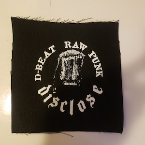 Könnte beinhalten: Schwarz-weiß gestickter Patch mit dem Text "D-Beat Raw Punk Disclose" in einem Kreis um eine Grafik eines Mikrofons.