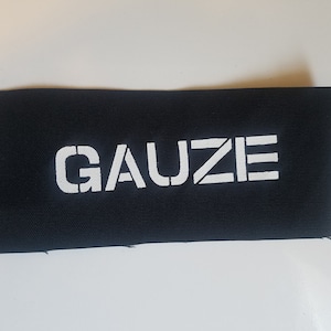 Op de afbeelding: Een zwarte stoffen patch met het woord "GAUZE" in wit gedrukt.
