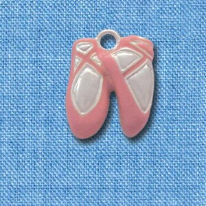 May include: A pink and white ballet slipper charm. The charm is approximately 2.5 cm in length. The charm has a loop at the top for attaching to a necklace or bracelet. The charm is set against a blue background.