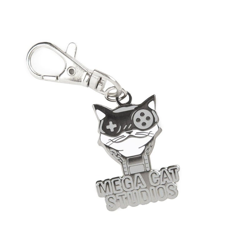 May include: Silver keychain featuring a cartoon cat wearing a video game controller over one eye. The cat's face is white with black eyes and a black nose. The keychain also has the text "MEGA CAT STUDIOS" in silver.