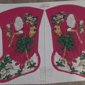 May include: A pair of red and white fabric panels with a Santa Claus stocking design. The stocking features a Santa Claus holding a Christmas tree and a bag of toys. The text "Santa's Stocking" is printed on the fabric.