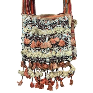 Könnte beinhalten: Dekorative Schultertasche mit strukturiertem Design. Die Tasche hat eine Mischung aus Farben, darunter Burgunder, Creme und Pfirsich, mit Pailletten und Quasten. Die Träger haben ein gestreiftes Design in Rot-, Orange- und Brauntönen.