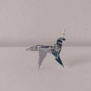 May include: A silver origami unicorn, folded from a single sheet of foil, stands on a white surface.
