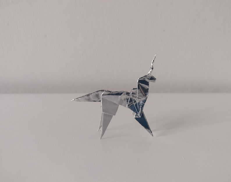 May include: A silver origami unicorn, folded from a single sheet of foil, stands on a white surface.