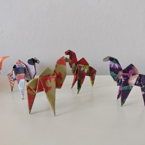 Peut inclure: Quatre chameaux en origami faits de papier à motifs colorés. Les chameaux sont debout sur une surface blanche.