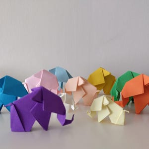 May include: A collection of colorful origami elephants in various hues, including blue, pink, yellow, green, and orange. The paper sculptures are arranged on a white surface, showcasing their detailed folds and forms. A creative and artistic display.