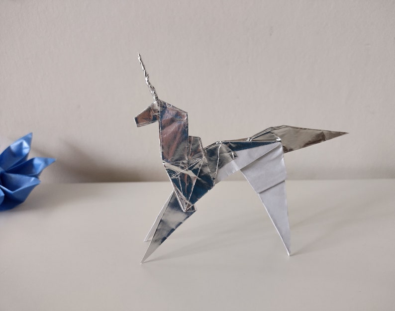 May include: A silver origami unicorn with a pointed horn, standing on a white surface.